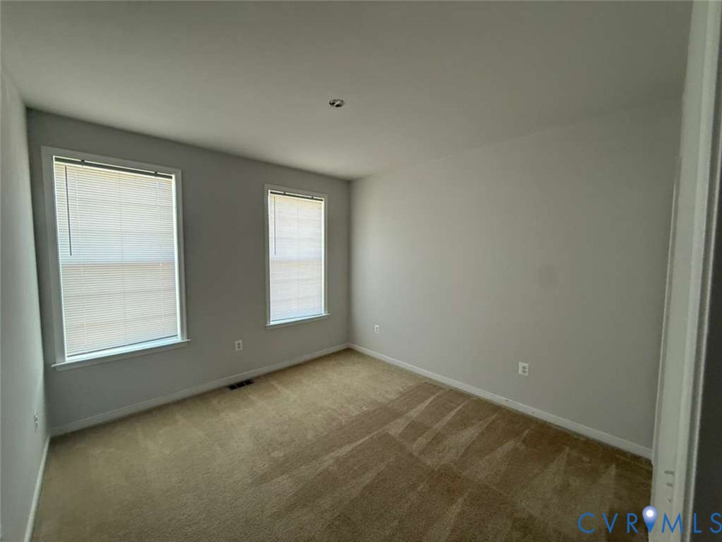 Neutral interior space featuring carpeting, light-toned wall finishes, two windows with integrated blinds, and ceiling-mounted lighting