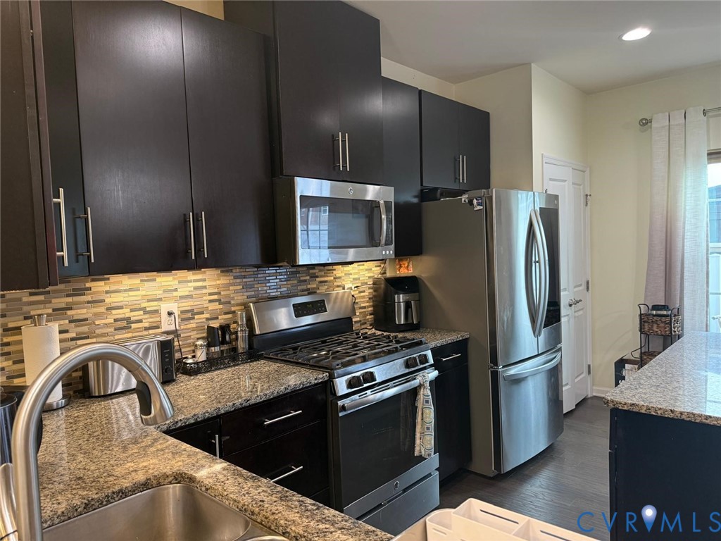 Kitchen featuring dark cabinetry, stone-finish countertops, stainless steel appliances, and a horizontal tile backsplash