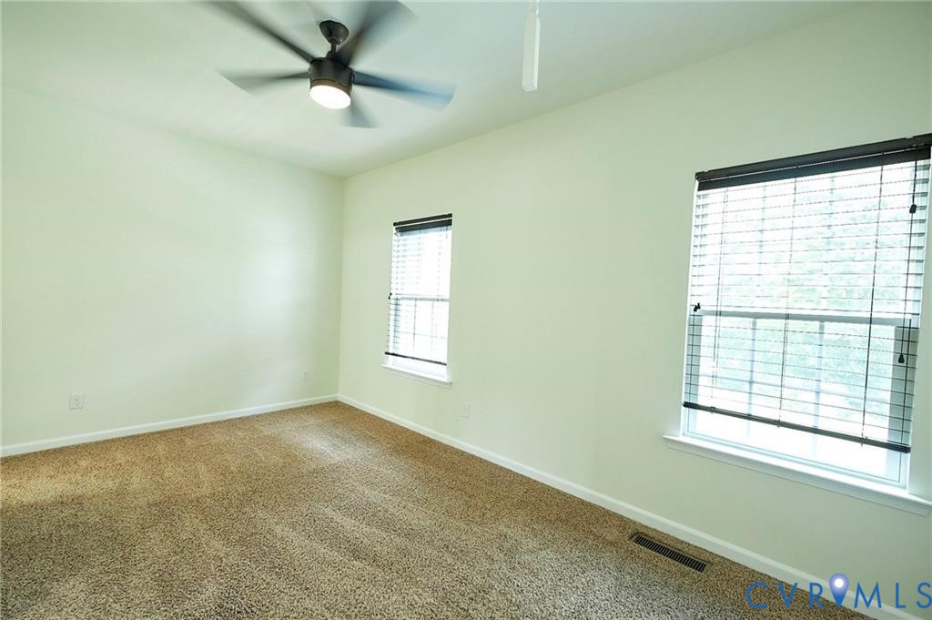 Room featuring wall-to-wall carpeting, dual windows with horizontal blinds, and a ceiling fan with integrated lighting