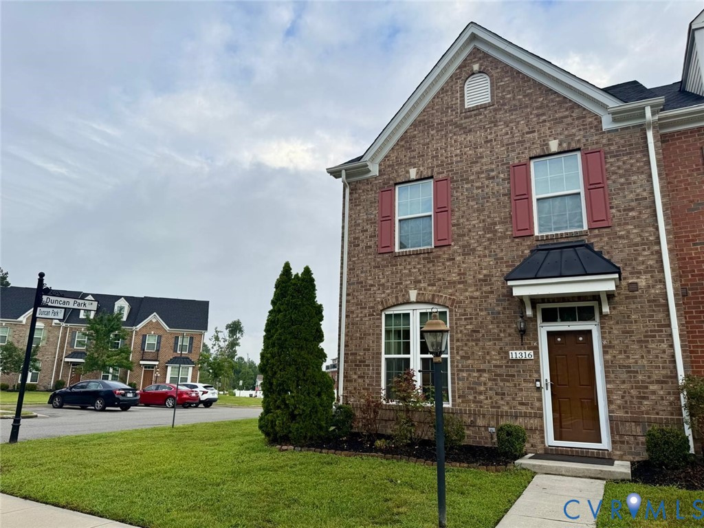 Brick exterior featuring a gabled roofline, decorative window shutters, metal door hood, and transom window above the entrance