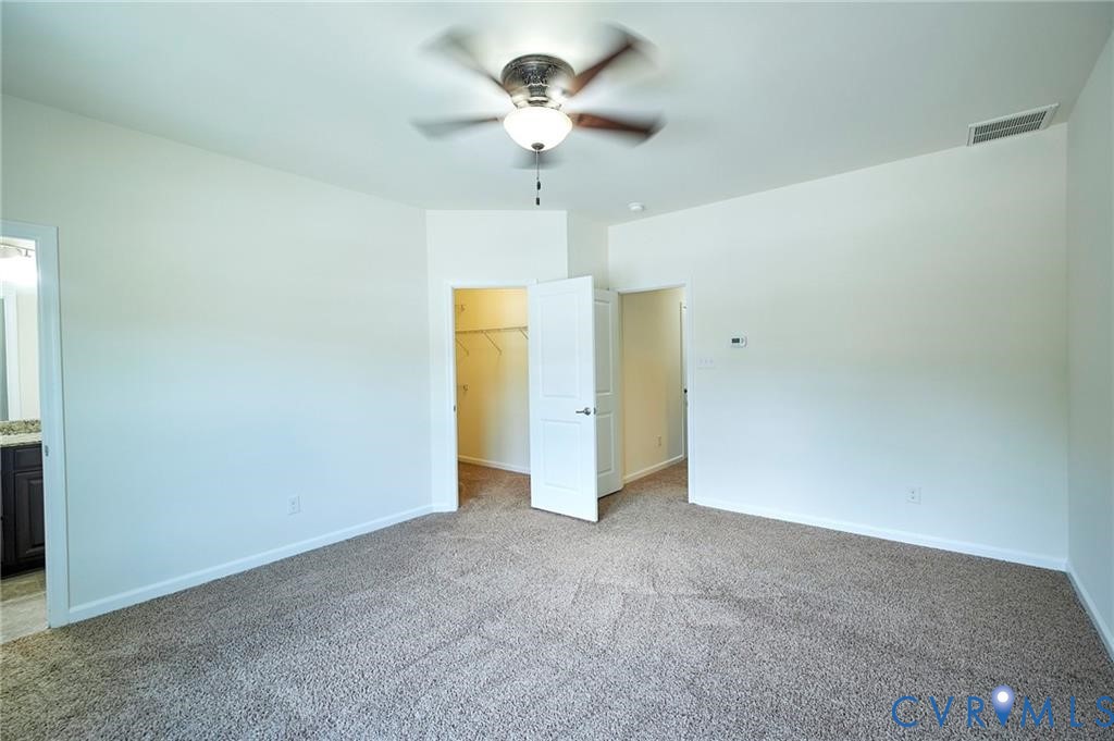 Neutral wall tones, wall-to-wall carpeting, ceiling fan with integrated lighting, and a walk-in closet with built-in shelving