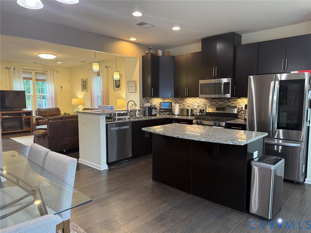 Kitchen featuring dark cabinetry, stone-surface countertops, center island, stainless steel appliances, and wood-finish flooring