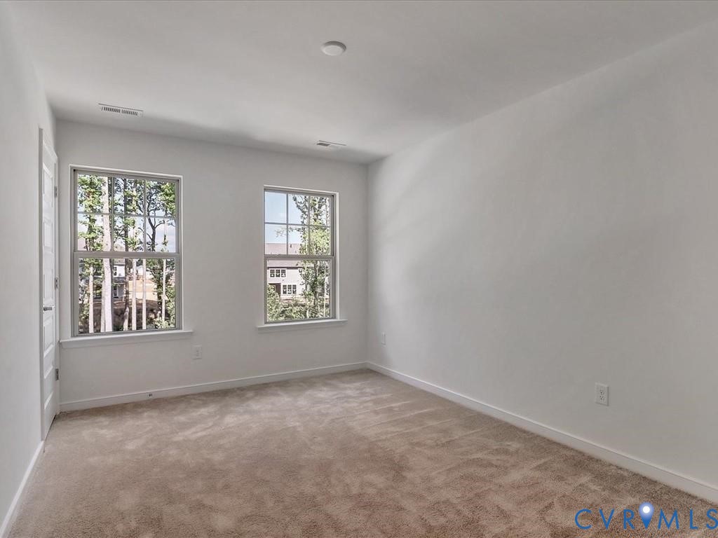 Neutral interior space featuring wall-to-wall carpeting, dual double-hung windows with muntins, and a solid-core interior door Neutral interior space featuring wall-to-wall carpeting, dual double-hung windows with muntins, and a solid-core interior door