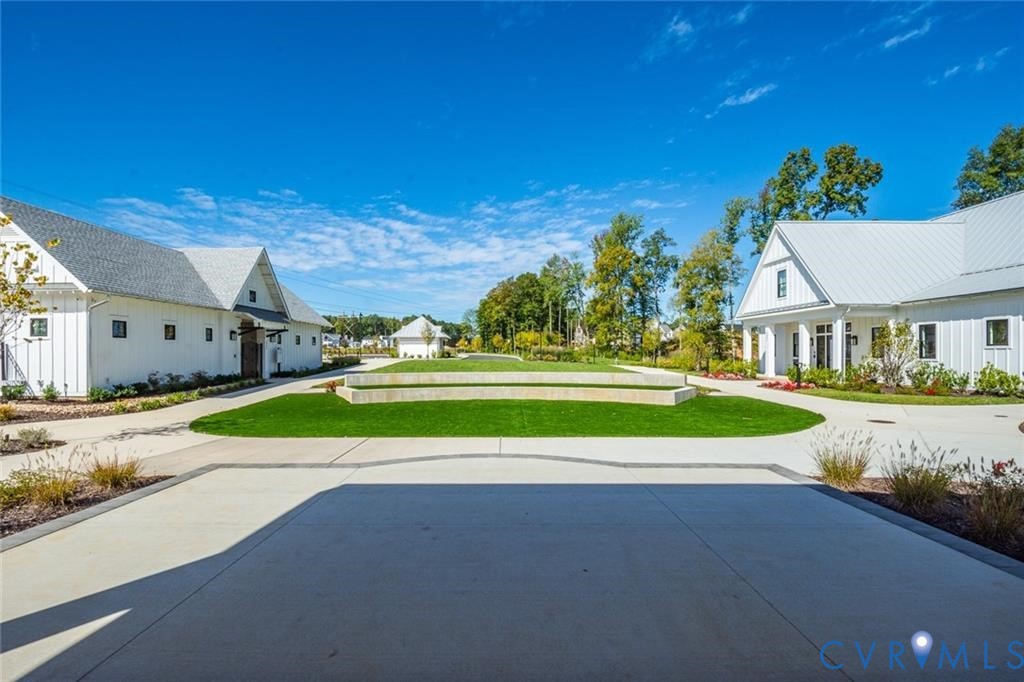 Modern farmhouse-style exteriors with vertical siding and metal roofing, central manicured lawn, stone retaining wall, and expansive paved courtyard