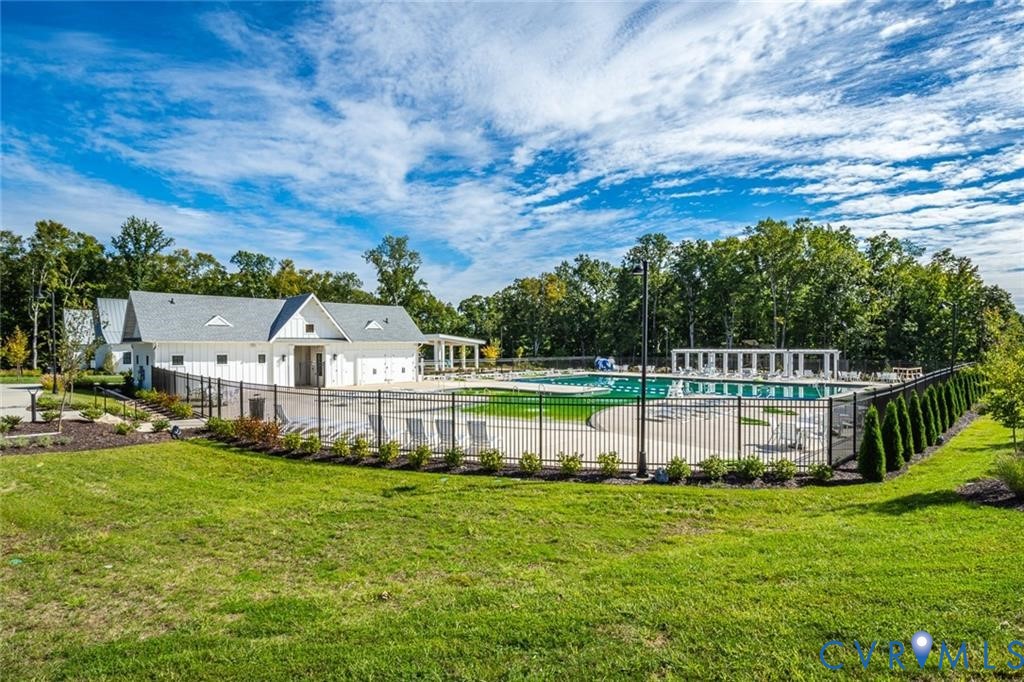 Swimming pool enclosed by black metal fencing, featuring a concrete pool deck, attached pool house, and a pergola-covered patio area