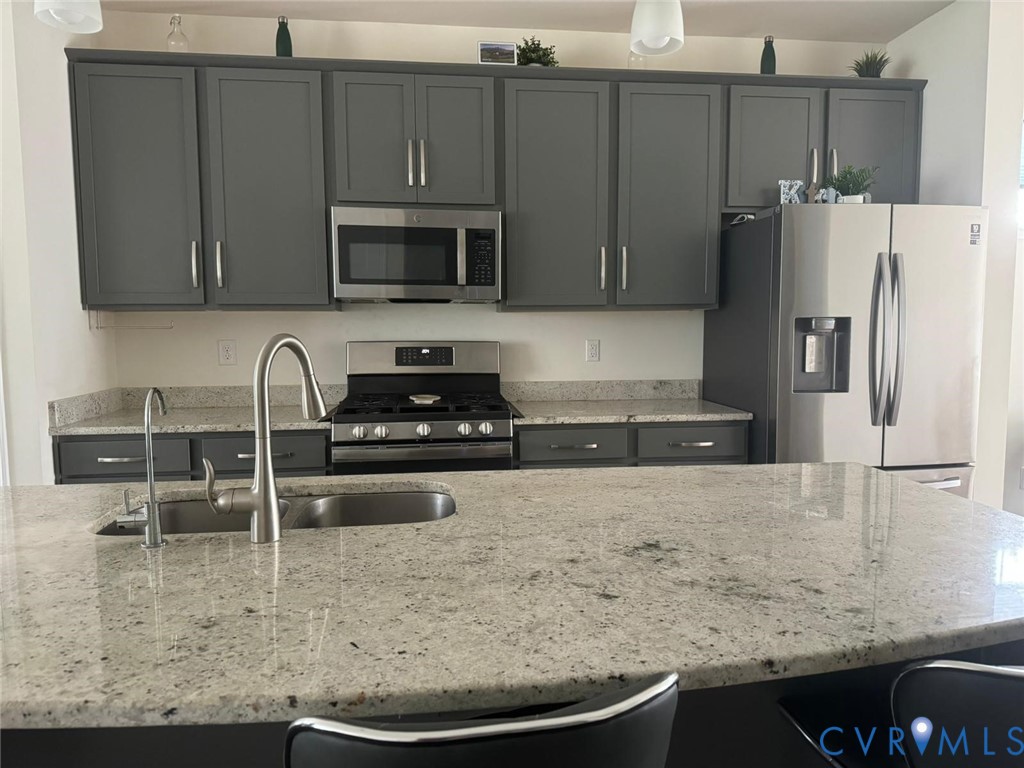 Kitchen featuring stone countertops, dark cabinetry, stainless steel appliances, a gas range, and a dual-basin undermount sink with a high-arch faucet Kitchen featuring stone countertops, dark cabinetry, stainless steel appliances, a gas range, and a dual-basin undermount sink with a high-arch faucet
