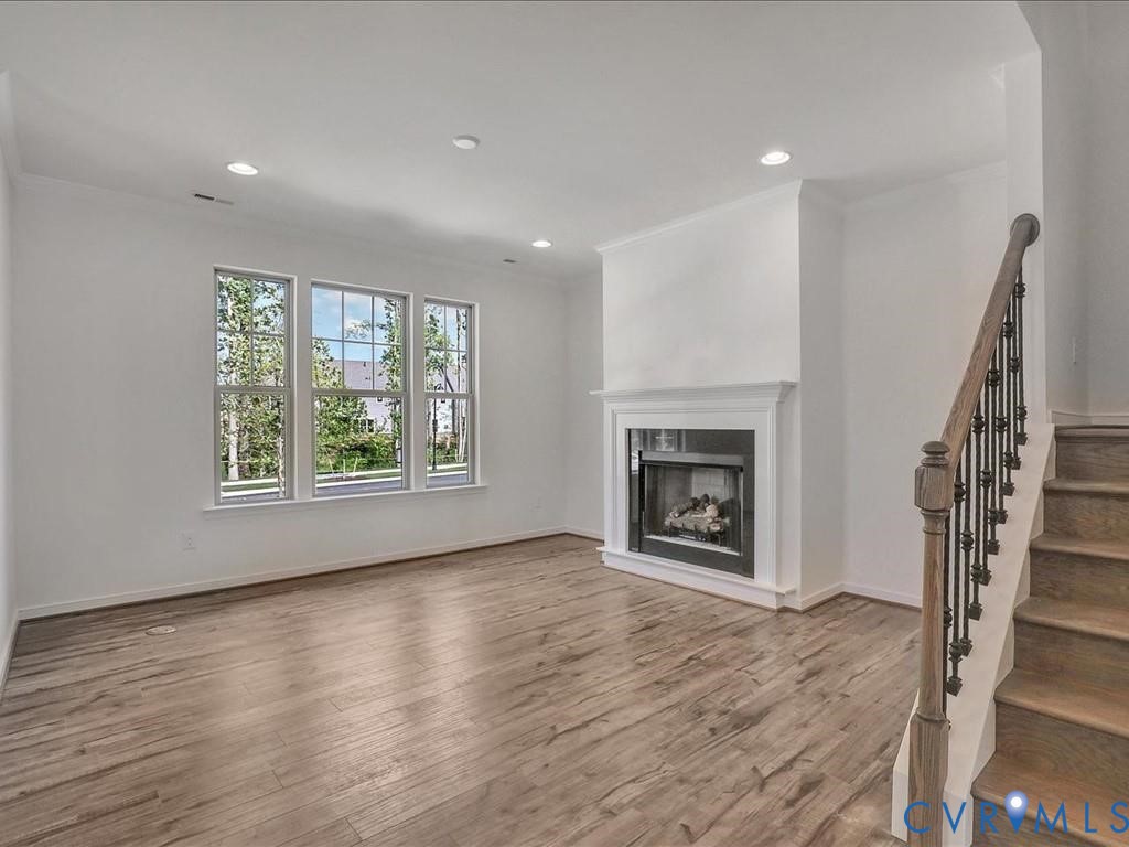 Living area featuring wood-finish flooring, recessed lighting, a fireplace with a white mantel, and a staircase with a wooden handrail and metal balusters