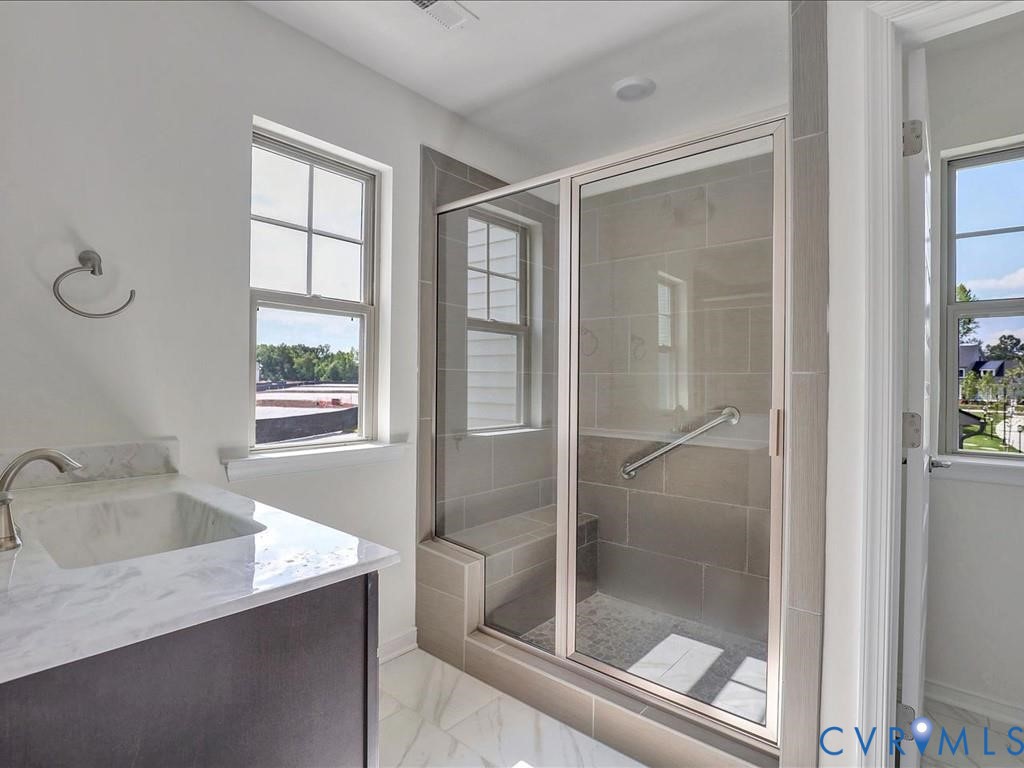 Vanity with stone-surface countertop, under-mount sink, chrome faucet, tiled walk-in shower with integrated bench and glass enclosure, and windows with multi-pane glazing Vanity with stone-surface countertop, under-mount sink, chrome faucet, tiled walk-in shower with integrated bench and glass enclosure, and windows with multi-pane glazing
