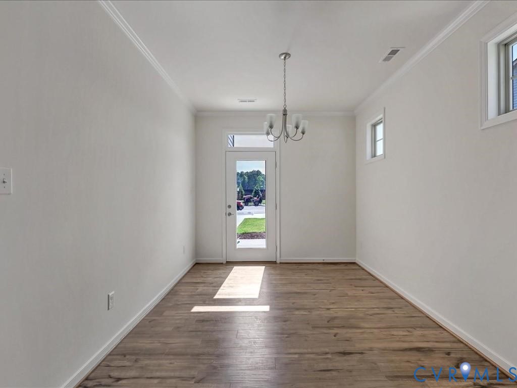 Interior space featuring wood-finish flooring, a multi-arm chandelier, crown molding, and a glass-panel entry door with a transom window