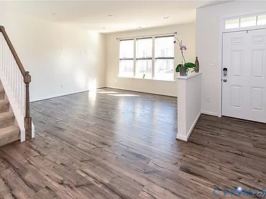 Wood-finish flooring, staircase with a wood-finish handrail, multi-pane windows, and white six-panel entry door with transom window