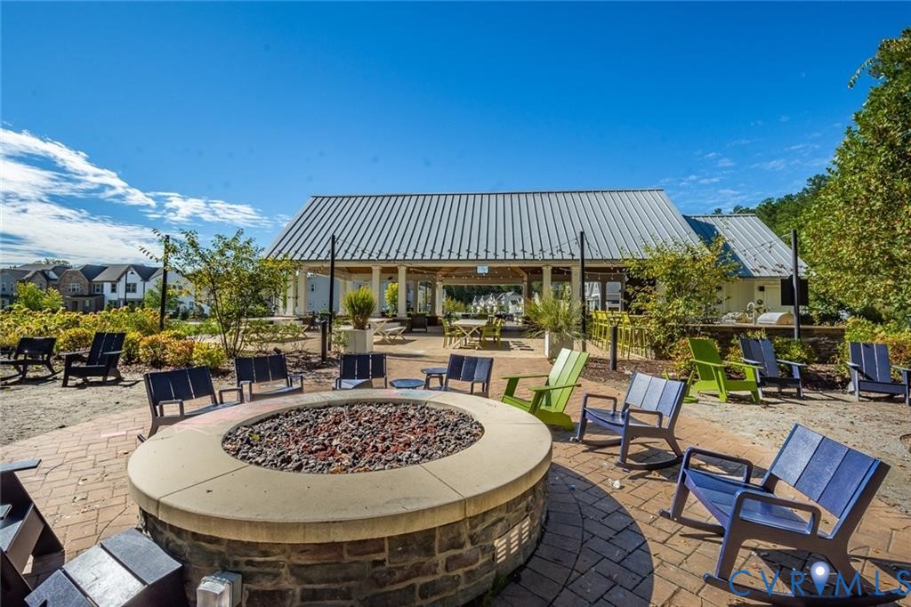 Outdoor community pavilion featuring a metal roof, stone-clad circular fire pit with a concrete cap, and paver hardscaping