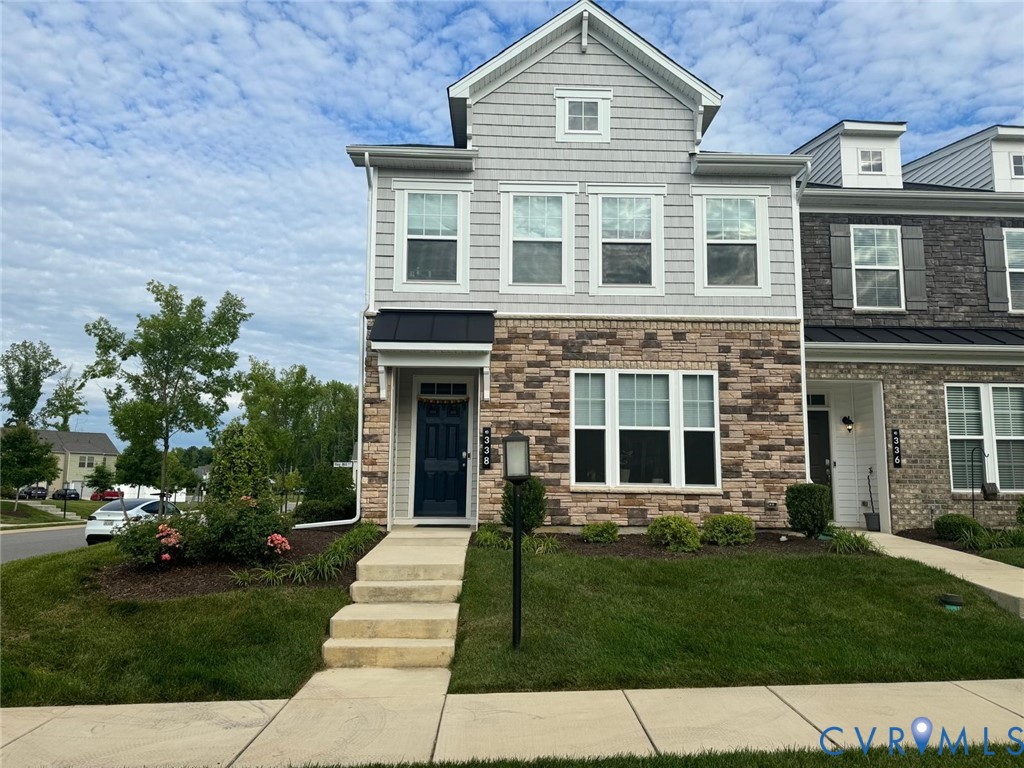 Multi-story townhome exterior featuring stone veneer siding, horizontal lap and shingle siding, a metal-roofed entryway awning, and multi-pane windows Multi-story townhome exterior featuring stone veneer siding, horizontal lap and shingle siding, a metal-roofed entryway awning, and multi-pane windows