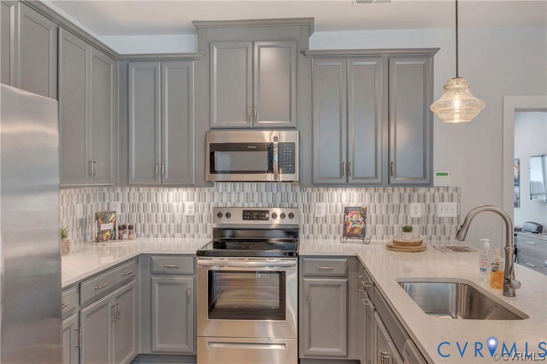 Kitchen featuring gray shaker-style cabinetry, quartz countertops, a patterned tile backsplash, stainless steel appliances, and a pendant light fixture Kitchen featuring gray shaker-style cabinetry, quartz countertops, a patterned tile backsplash, stainless steel appliances, and a pendant light fixture