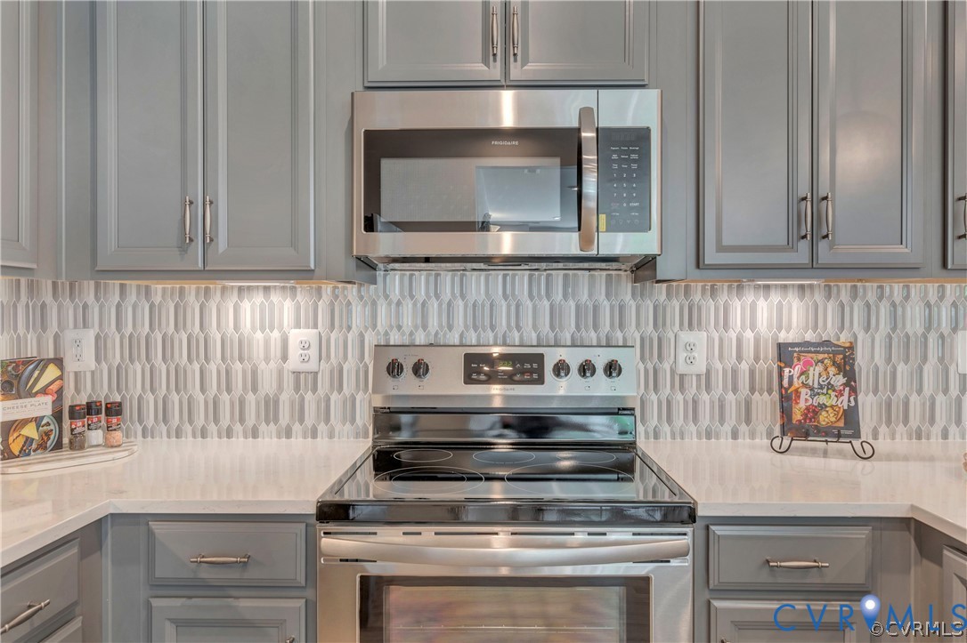 Shaker-style cabinetry, stainless steel microwave, glass-top range, quartz countertops, and a decorative picket-pattern tile backsplash Shaker-style cabinetry, stainless steel microwave, glass-top range, quartz countertops, and a decorative picket-pattern tile backsplash