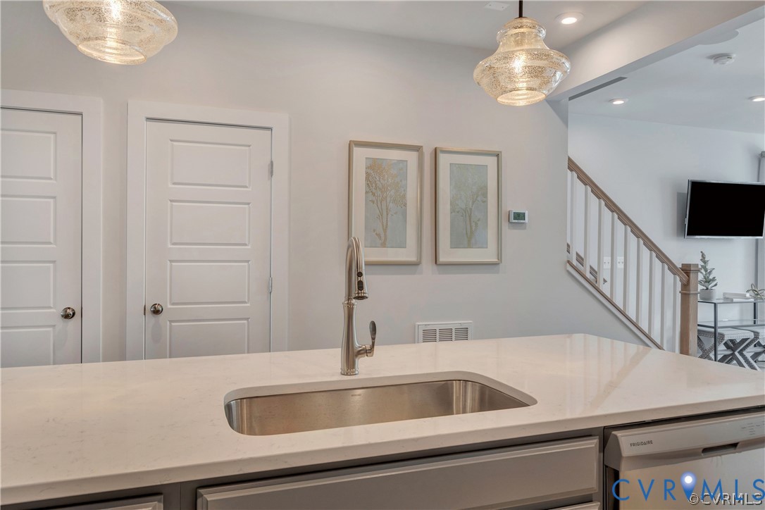 Kitchen island featuring a solid-surface countertop, under-mount stainless steel sink, gooseneck pull-down faucet, and decorative pendant lighting Kitchen island featuring a solid-surface countertop, under-mount stainless steel sink, gooseneck pull-down faucet, and decorative pendant lighting