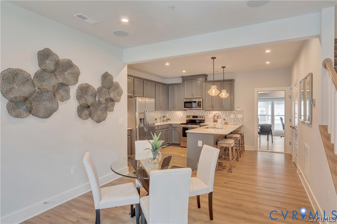 Kitchen featuring grey cabinetry, stone-finish countertops, stainless steel appliances, a central island with bar seating, and wood-finish flooring Kitchen featuring grey cabinetry, stone-finish countertops, stainless steel appliances, a central island with bar seating, and wood-finish flooring