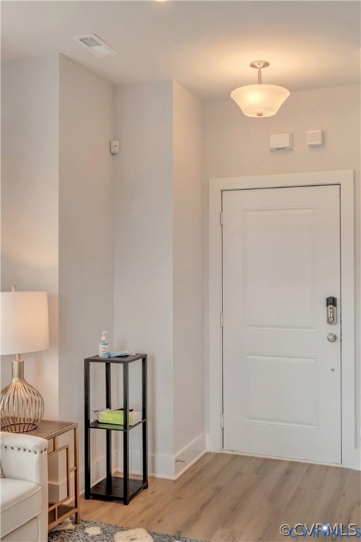 Entryway featuring a white paneled door with electronic deadbolt, neutral wall color, and wood-finish flooring complemented by a semi-flush mount bowl light fixture