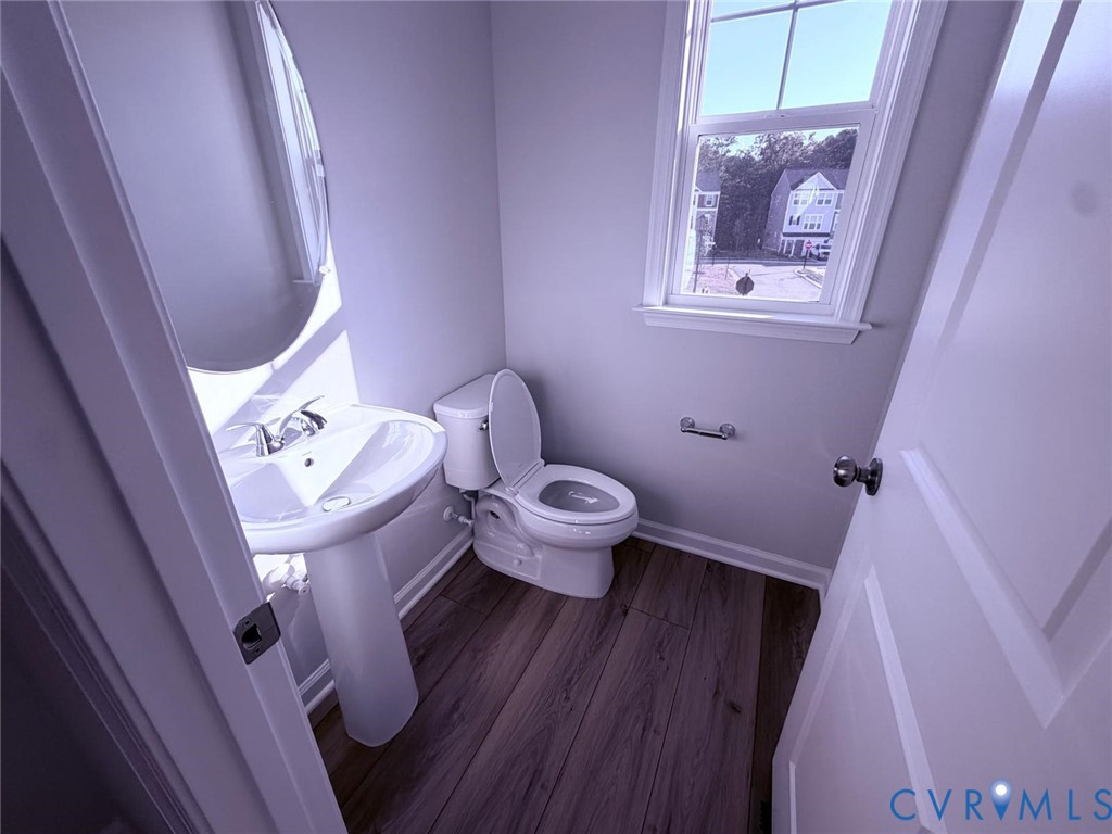 Pedestal sink with polished chrome faucet, wood-finish flooring, dual-flush toilet, oval wall-mounted mirror, and multi-pane window