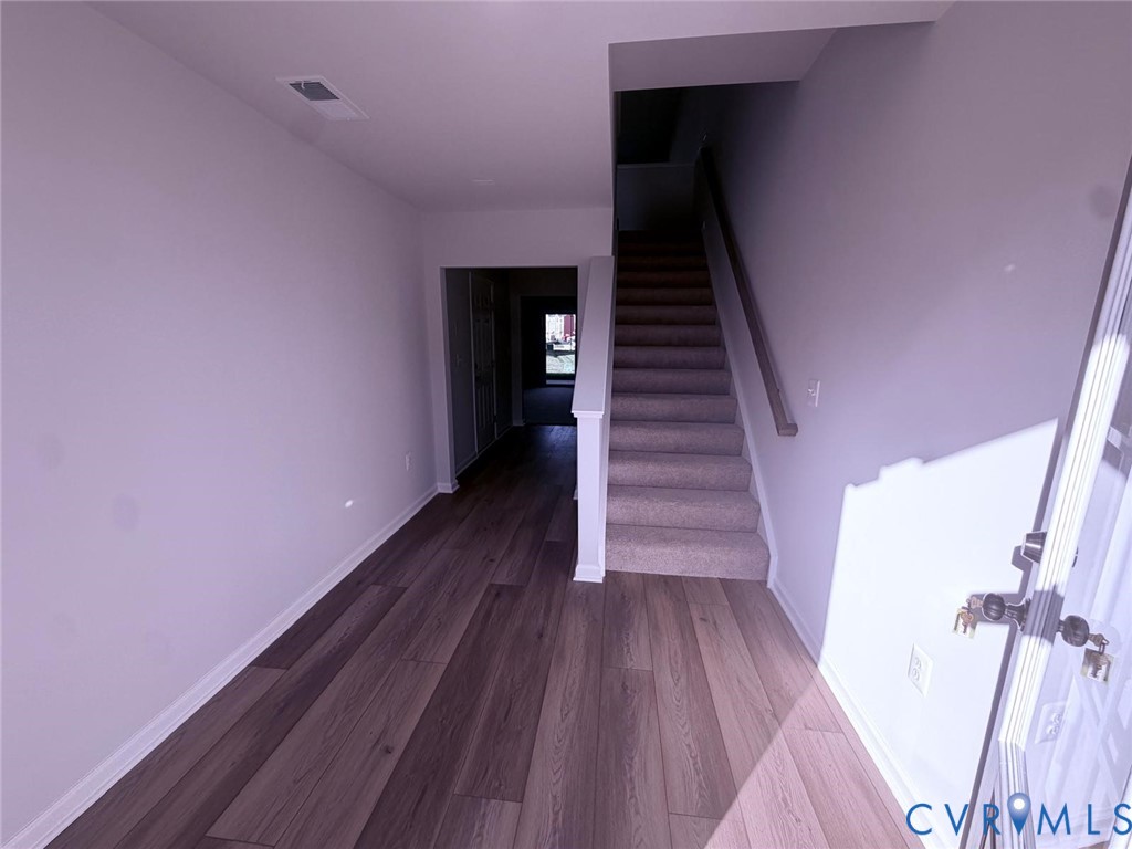 Entryway featuring wood-finish flooring, a carpeted staircase with a wooden handrail, and neutral wall paint Entryway featuring wood-finish flooring, a carpeted staircase with a wooden handrail, and neutral wall paint