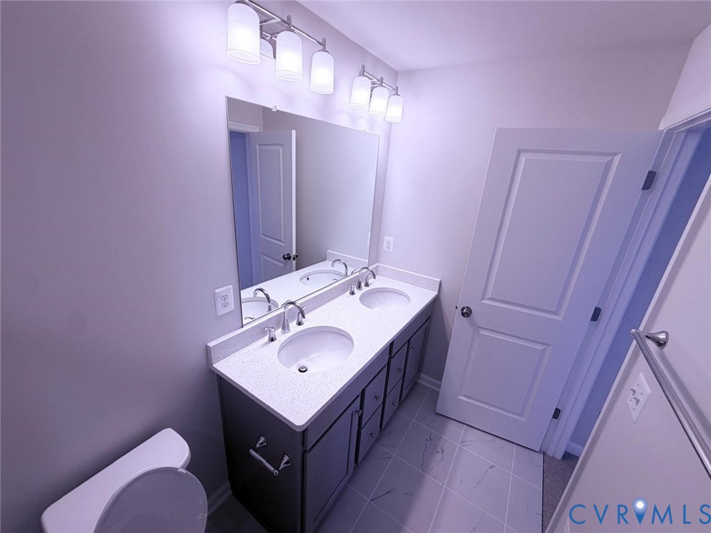 Double vanity featuring a light-toned countertop with integrated dual basins, dark cabinetry, large wall-mounted mirror, and tile flooring