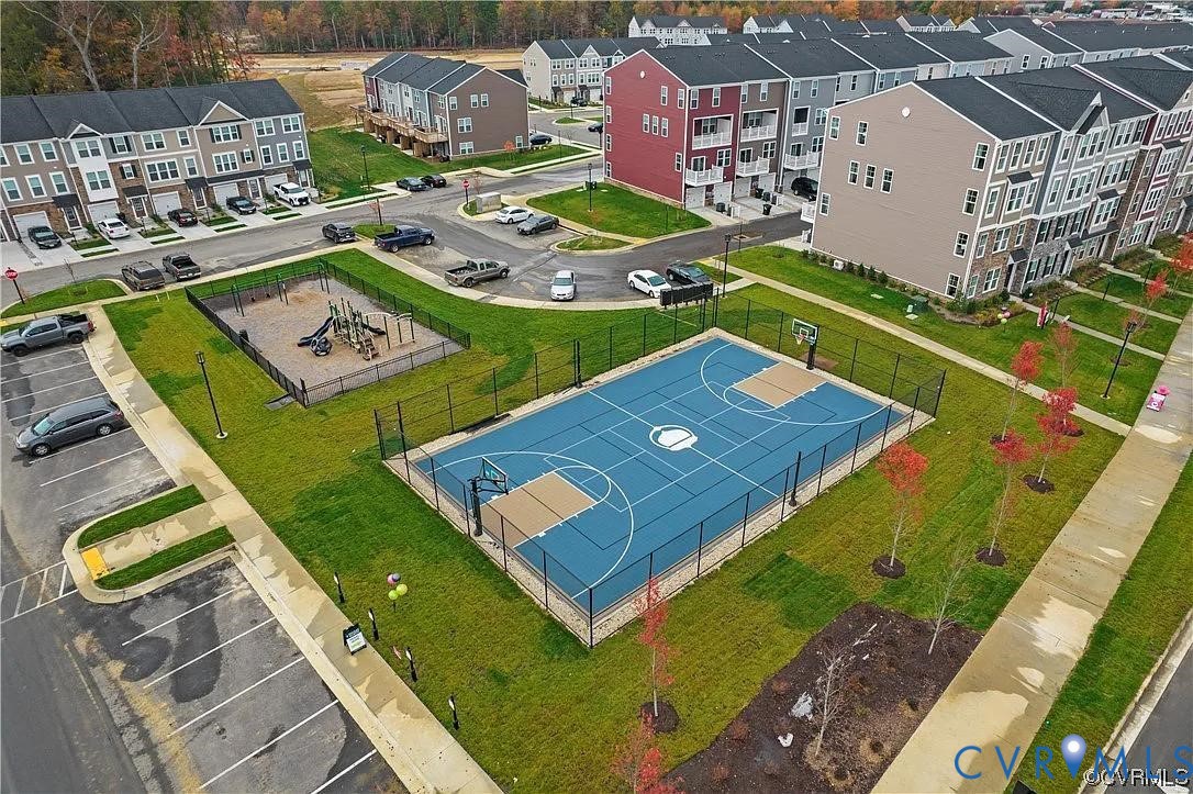 Community recreation area featuring a fenced basketball court with blue hardscaping, a designated playground, and surrounding paved parking