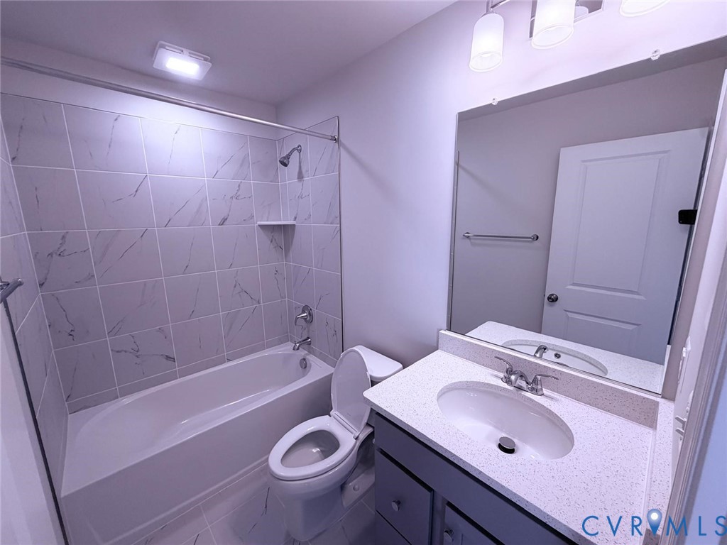 Bathroom featuring a tub-shower combination with floor-to-ceiling tile surround, a vanity with a quartz countertop, an integrated oval sink, and a large frameless mirror