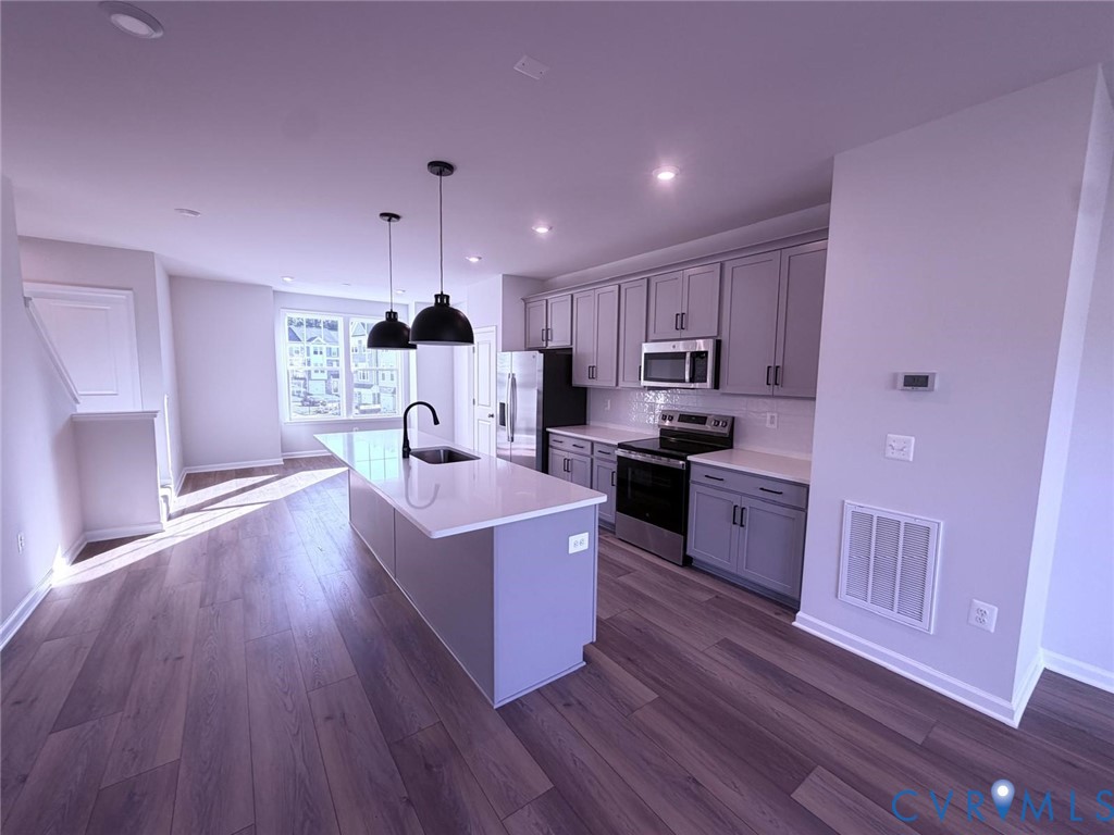 Kitchen featuring an oversized central island with stone-finish countertops, shaker-style cabinetry, stainless steel appliances, and wood-finish flooring