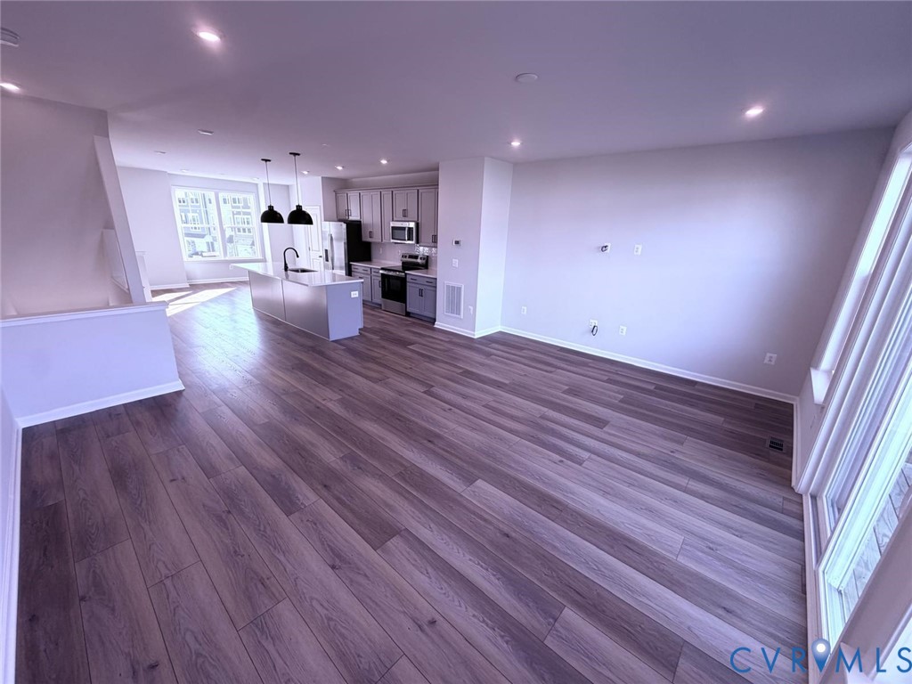 Open-concept interior featuring wood-finish flooring, a kitchen island with pendant lighting, shaker-style cabinetry, and large windows