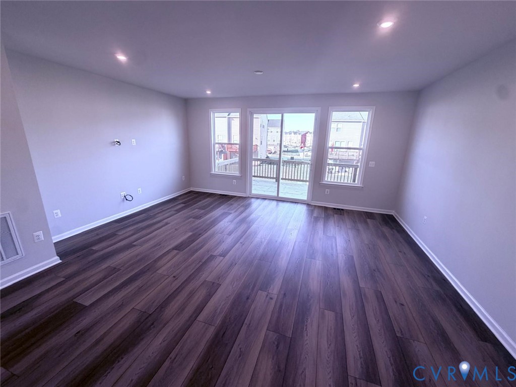 Open-concept room featuring wood-finish flooring, recessed lighting, double-hung windows, and sliding glass doors with exterior deck access Open-concept room featuring wood-finish flooring, recessed lighting, double-hung windows, and sliding glass doors with exterior deck access