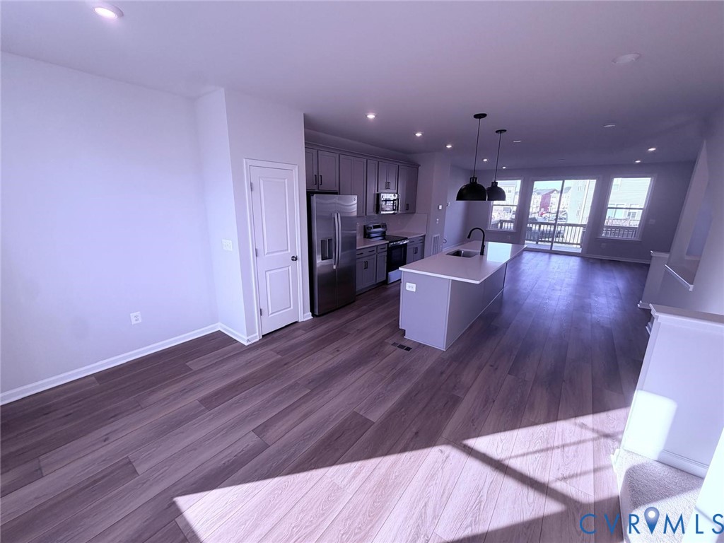 Kitchen featuring wood-finish flooring, stainless steel appliances, central island with light-toned countertop, pendant lighting, and sliding glass doors