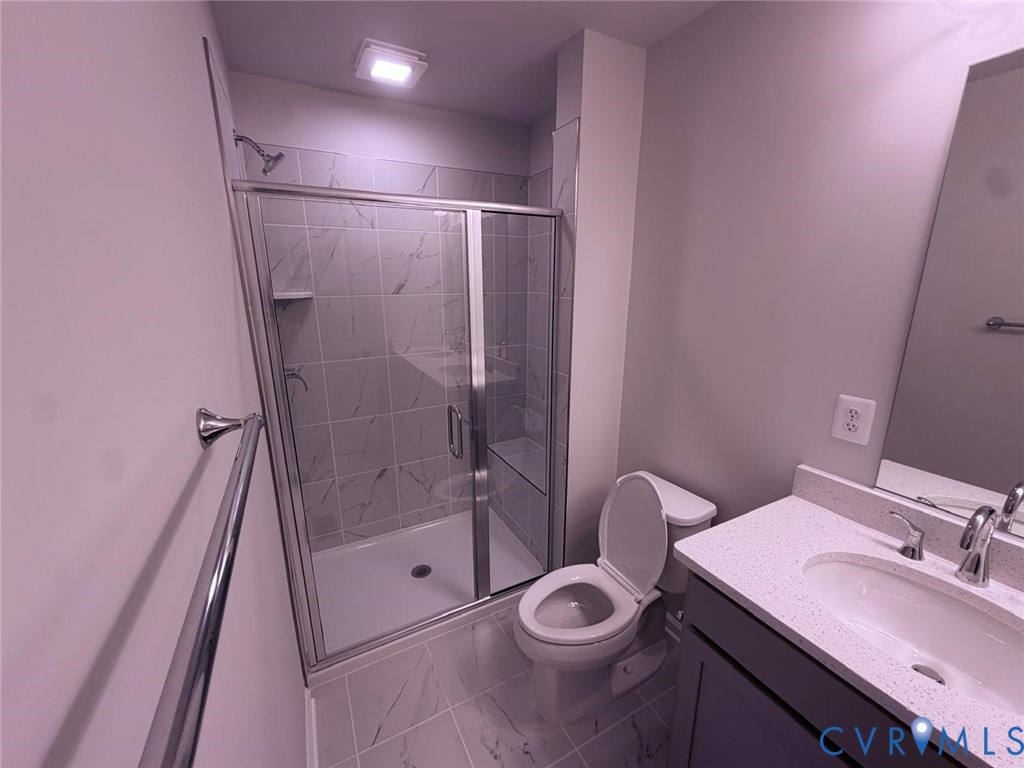 Bathroom featuring a shower with a chrome-framed glass enclosure, stone-finish tile surround, vanity with a light-toned quartz countertop, and large-format porcelain tile flooring