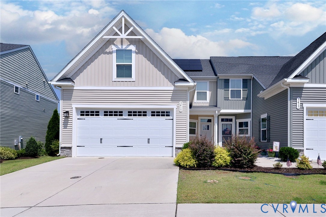Multi-story exterior featuring lap and vertical siding, a two-car garage with carriage-style doors, asphalt shingle roofing, integrated solar panels, and a concrete driveway