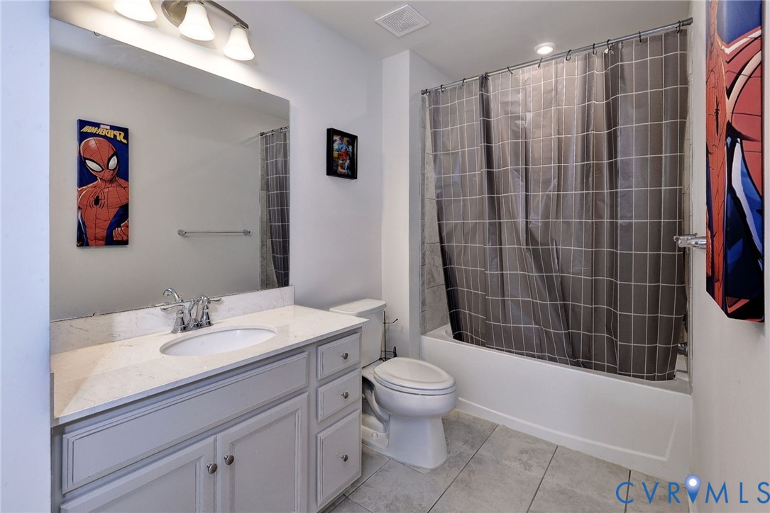 Bathroom featuring a vanity with stone-finish countertop, undermount sink, chrome faucet, large-format tile flooring, and a shower-tub combination