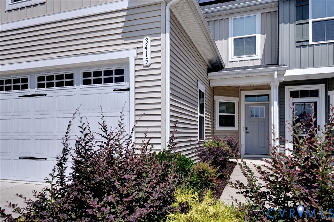 Exterior featuring light-colored horizontal siding, contrasting vertical siding accents, a panelled garage door with decorative hardware, and a covered entry with a glass-inset door