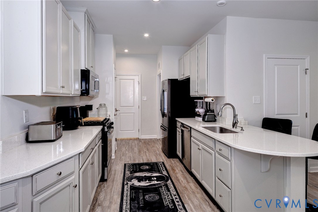Kitchen featuring white shaker-style cabinetry, solid-surface countertops, wood-finish flooring, a stainless steel undermount sink, and recessed lighting