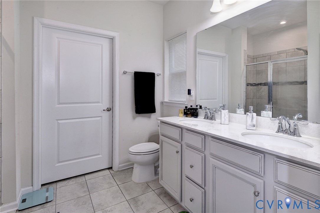 Bathroom featuring a dual-sink vanity with light-toned cabinetry, light-colored countertops, polished chrome fixtures, a large wall-mounted mirror, and tile flooring