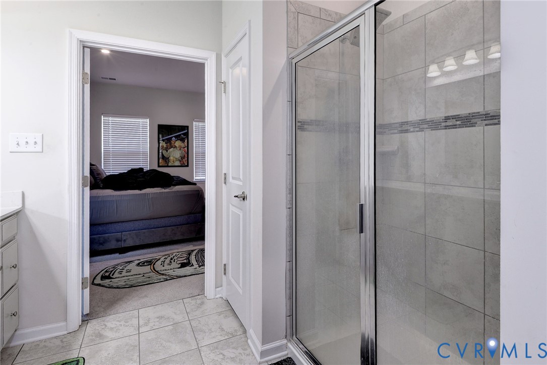 Walk-in shower featuring glass enclosure, large-format tile surround, and decorative glass mosaic accent tile, complemented by ceramic tile flooring