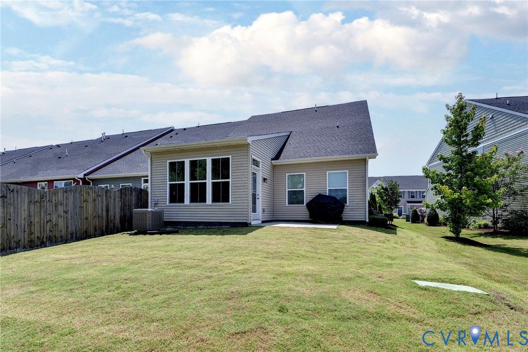 Rear exterior featuring light-toned horizontal siding, dark shingle roofing, multi-pane windows, and a fenced-in grassy yard