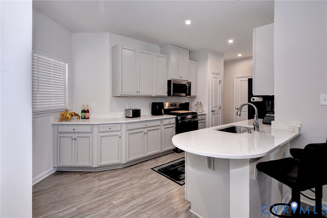 Kitchen featuring white cabinetry, solid surface countertops, a curved peninsula, stainless steel undermount sink, and wood-finish flooring