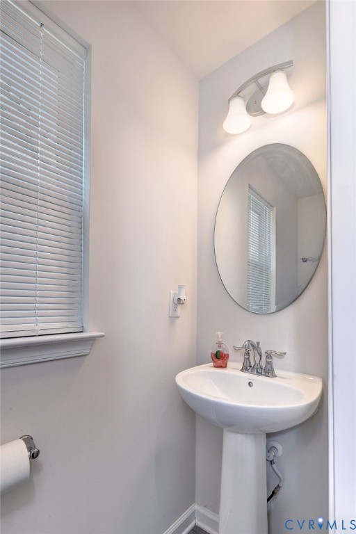 White pedestal sink with a polished chrome dual-handle faucet, oval wall-mounted mirror, and dual-shade vanity light fixture