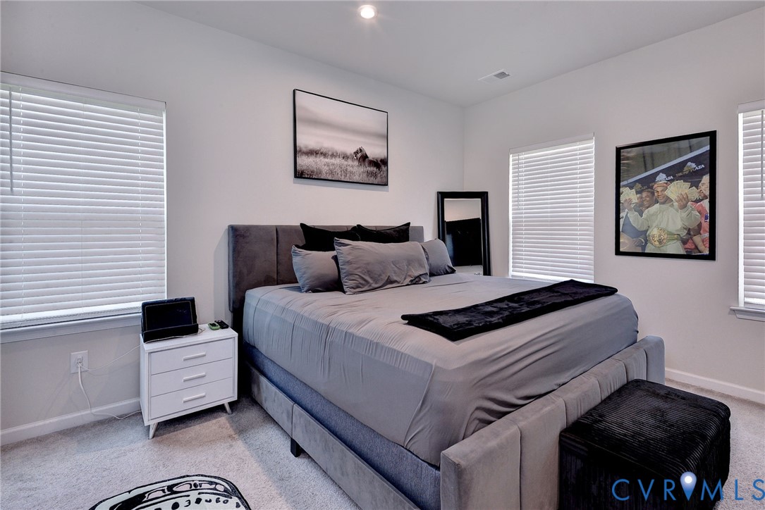 Neutral-toned interior room with wall-to-wall carpeting, recessed ceiling lighting, and three windows equipped with horizontal blinds