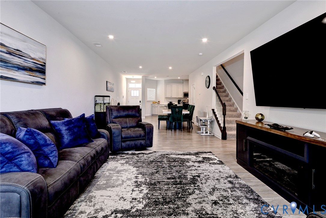 Neutral interior featuring wood-finish flooring, recessed lighting, a built-in electric fireplace console, and a staircase with a wooden handrail and balusters