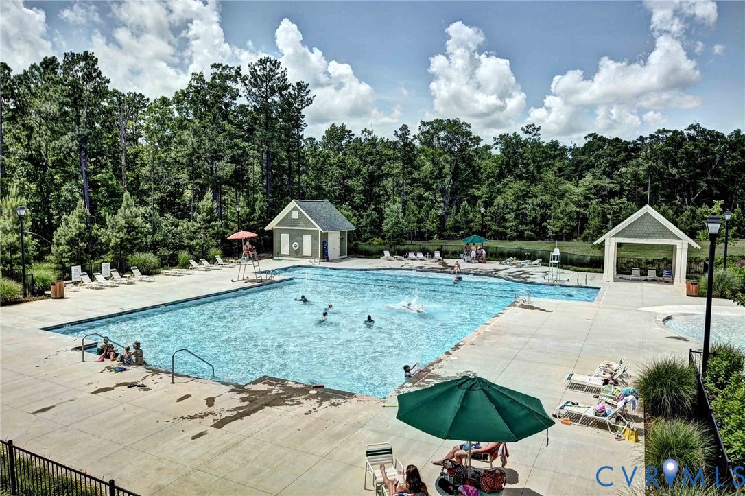 Swimming pool featuring concrete decking, a surrounding metal fence, and two covered structures