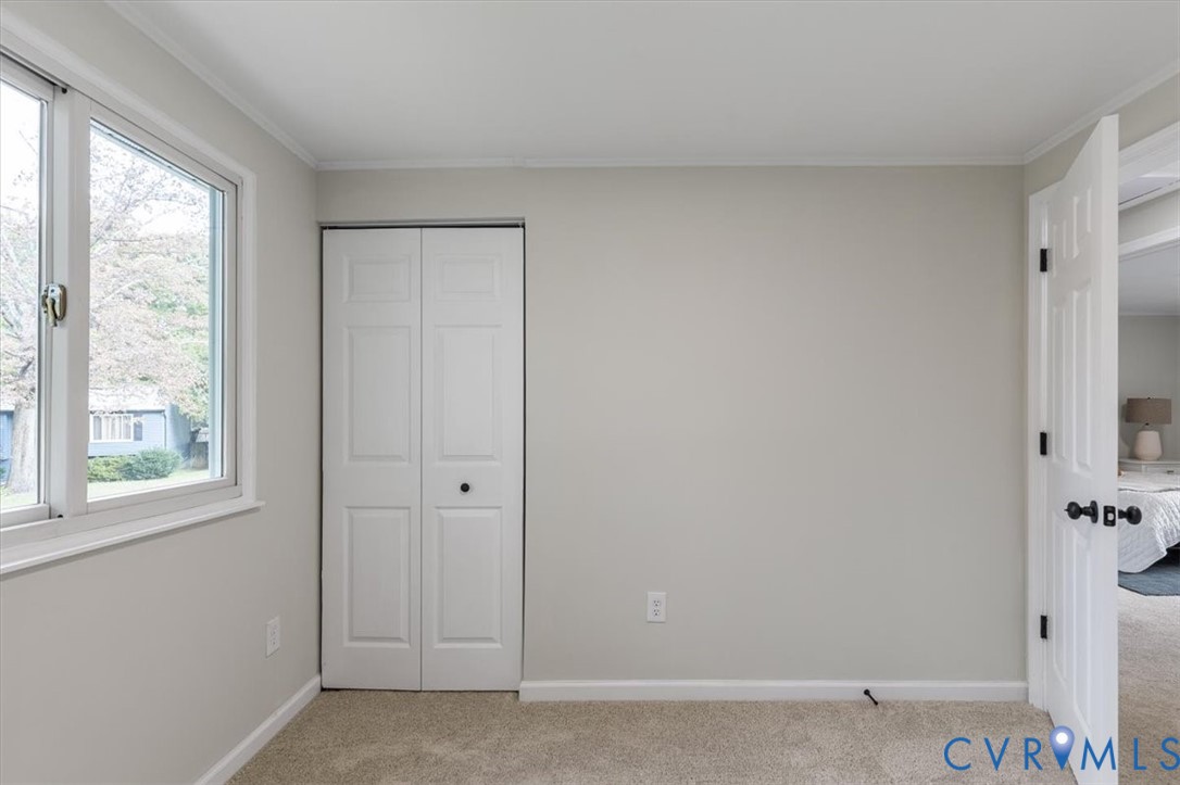 Neutral-toned walls, double-hung window, bi-fold closet doors, and carpeted flooring