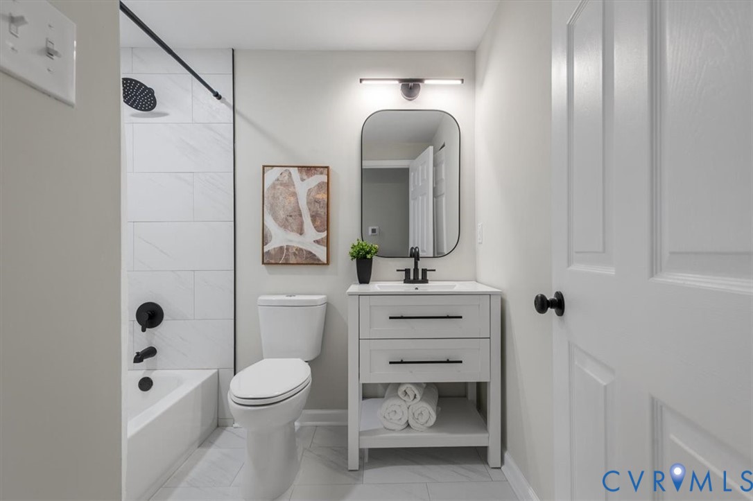 Bathroom featuring a white vanity with two drawers, an arched mirror, matte black fixtures, and a tub enclosure with large-format tile surround