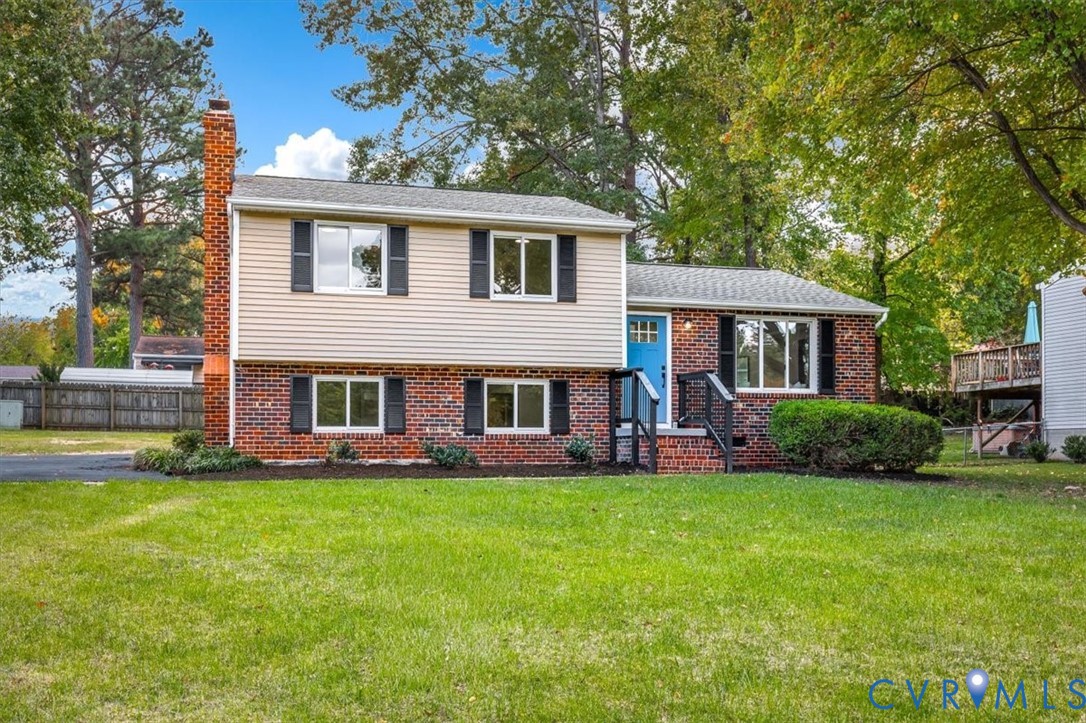 Split-level exterior featuring a brick and vinyl facade, exterior brick chimney, dual-tone siding, and an asphalt driveway