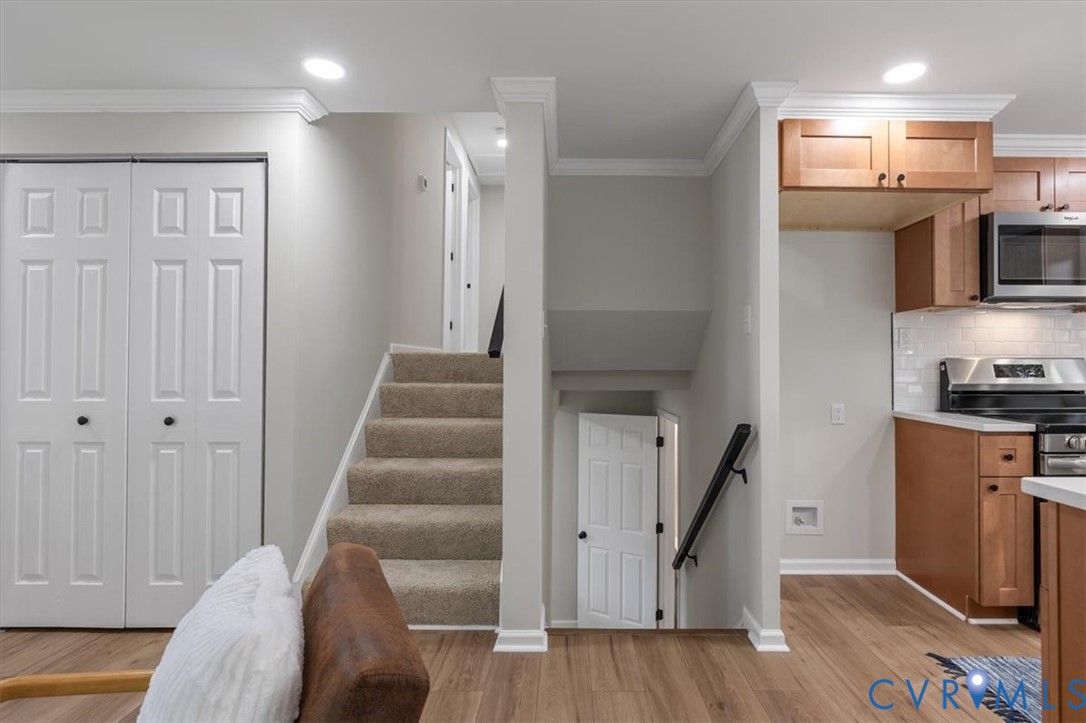 Kitchen featuring wood cabinetry, stainless steel appliances, and subway tile backsplash, complemented by wood-finish flooring, recessed lighting, and crown molding