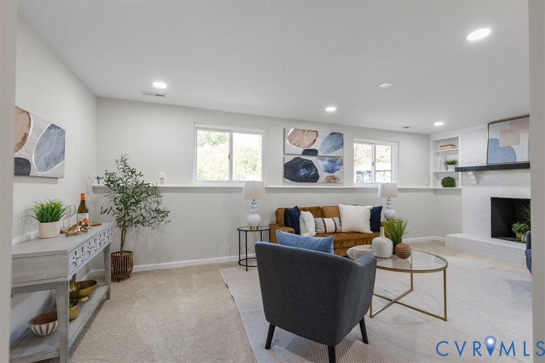 Living area featuring neutral carpeting, recessed lighting, horizontal windows with integrated sills, and a fireplace with a white brick surround and wood mantel