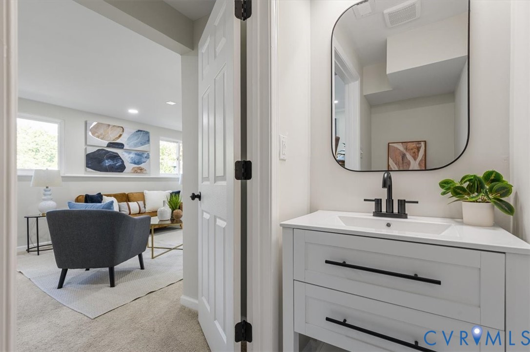 White vanity featuring quartz countertop, rectangular basin, matte black faucet, and hardware, complemented by a rounded mirror