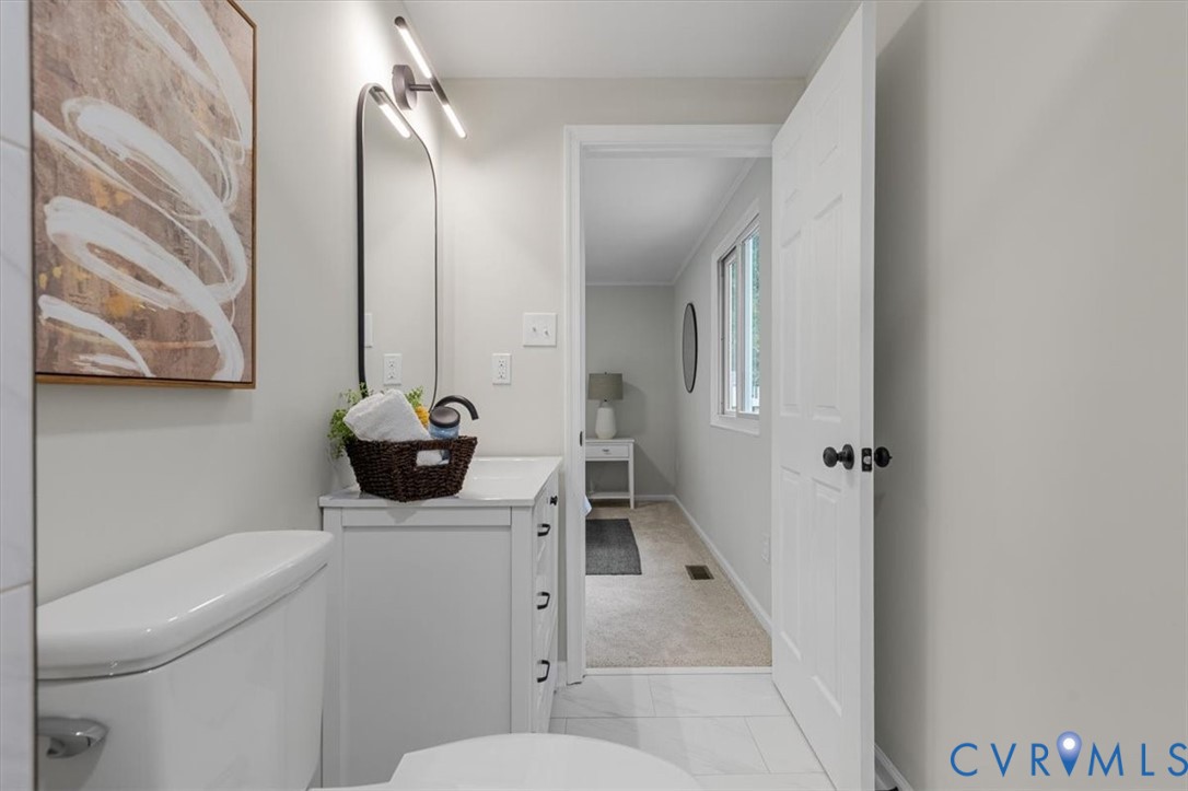 White vanity cabinet with integrated countertop, arched wall-mounted mirror, minimalist light fixture, and tile flooring